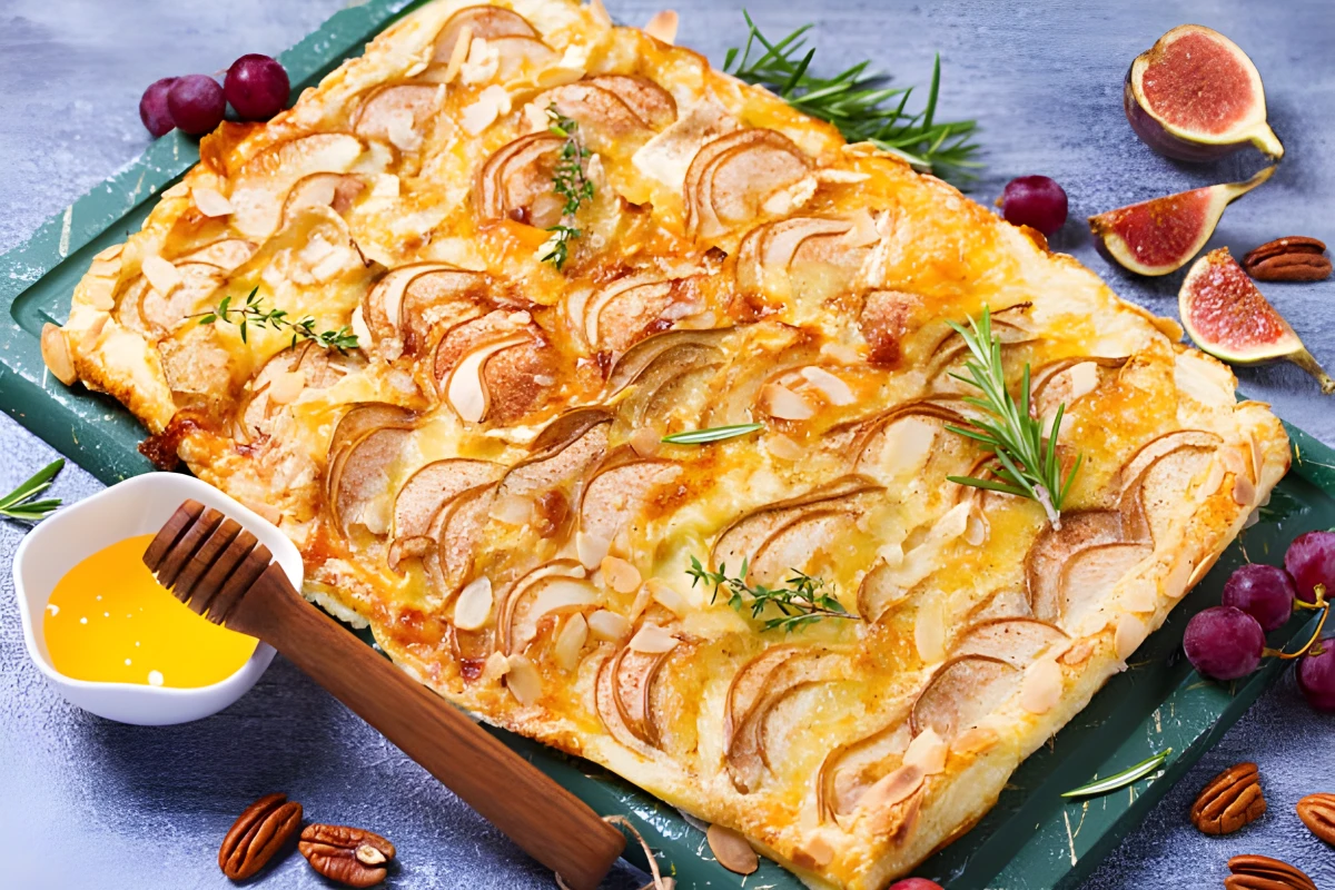 Tarte feuilletée rectangulaire aux poires tranchées, brie fondant, amandes dorées et herbes fraîches.
